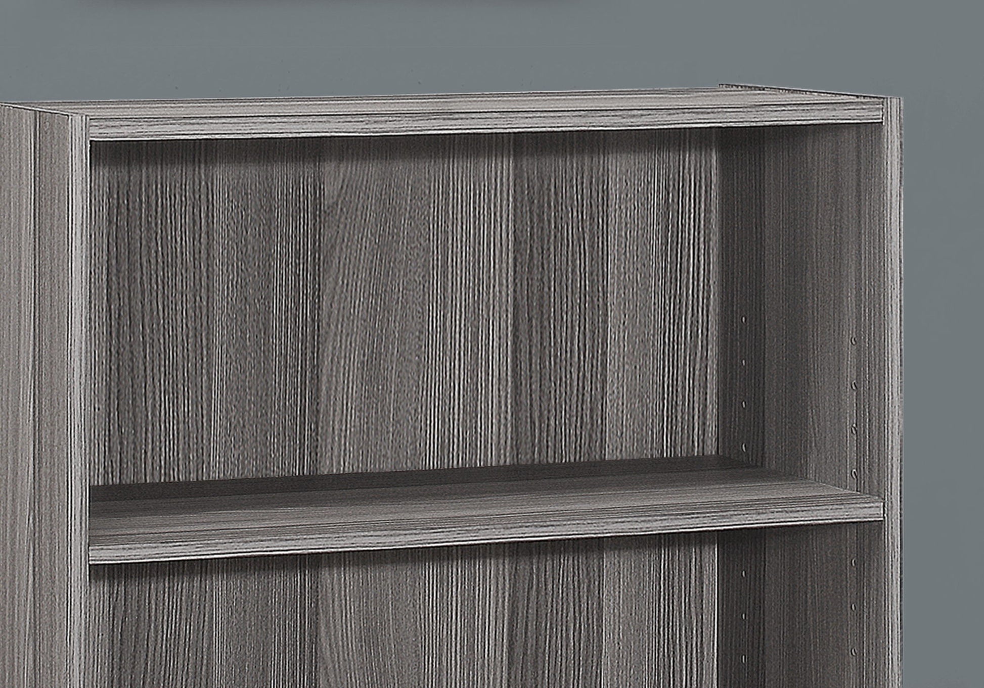 A close-up of a gray, 4-tier bookshelf with a modern, wood grain texture and transitional design, ideal for office use, set against a plain gray background.