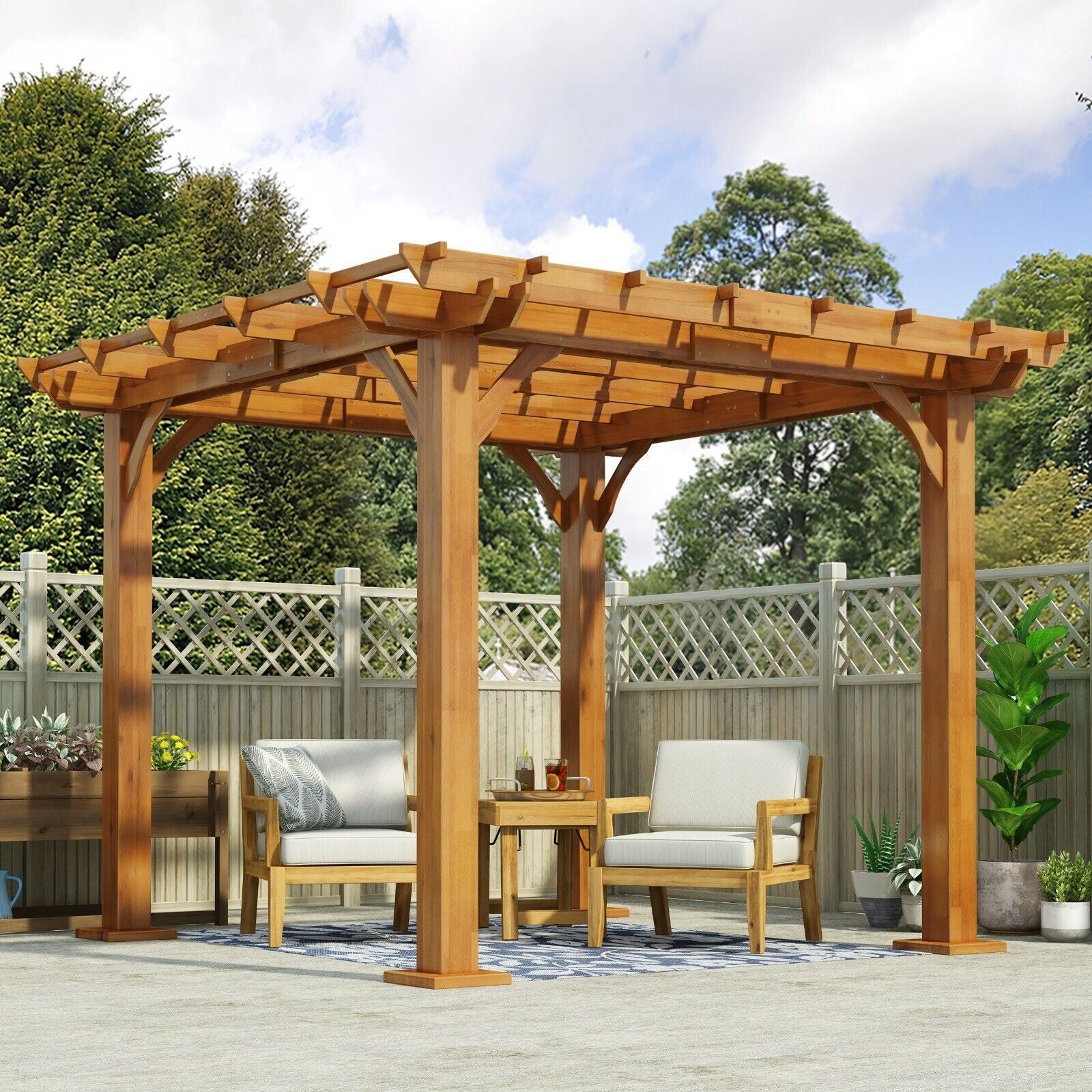 The Brady 10 x 10 Ft. Square Pergola in teak stands on a patio, sheltering two cushioned chairs and a small table, surrounded by a wooden fence with lattice panels and greenery in the background.