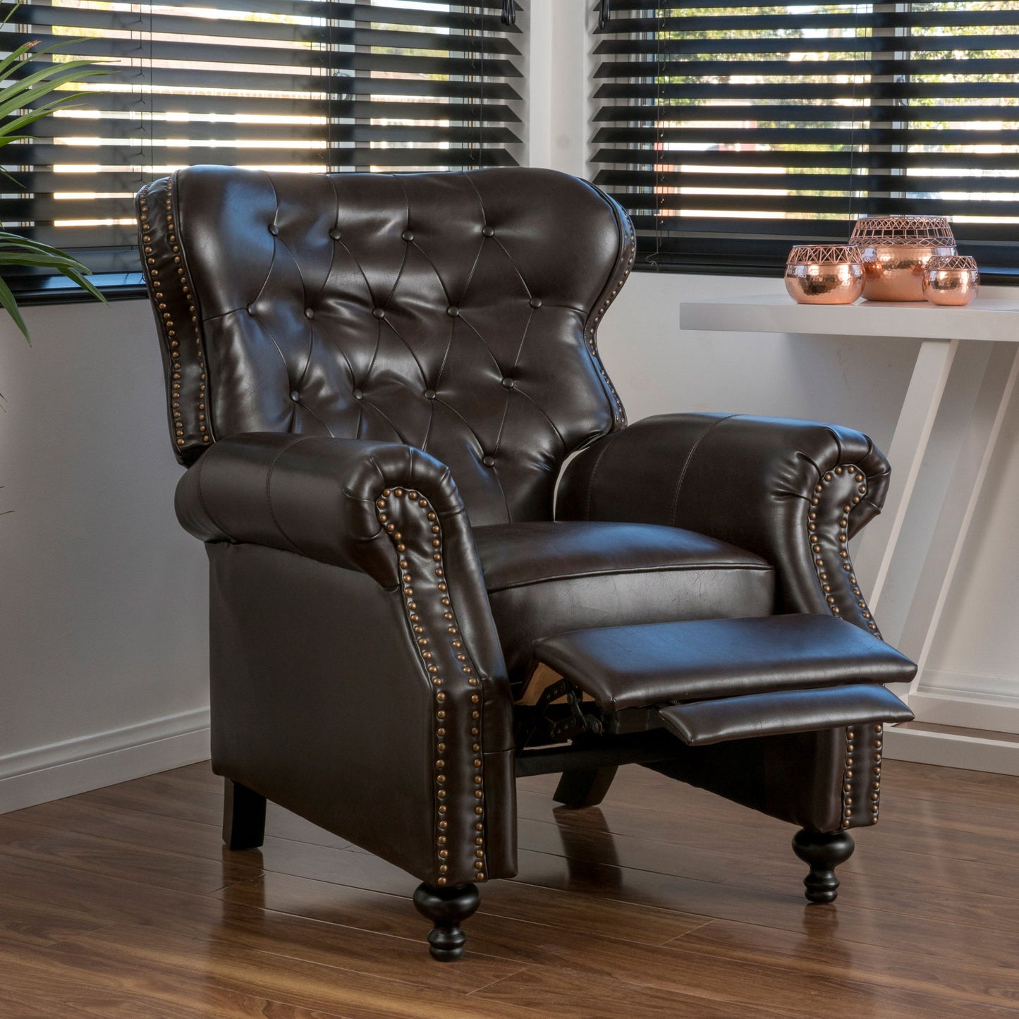 The Contemporary Style Push Back Recliner with button tufted stitching and nailhead trim, shown in a modern room with wood flooring, large windows, a white table, and decorative accents.