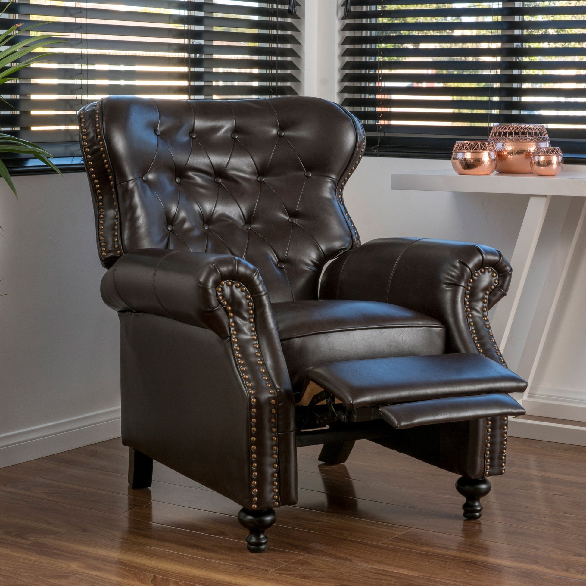 The Contemporary Style Push Back Recliner with button tufted stitching and nailhead trim, shown in a modern room with wood flooring, large windows, a white table, and decorative accents.