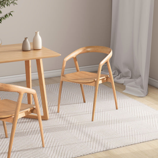A minimalist dining area featuring Simeon Scandinavian Sculpted Dining Chairs in warm natural brown around a light wood table on a textured white rug, with two ceramic vases, a neutral wall, and a draped white curtain.