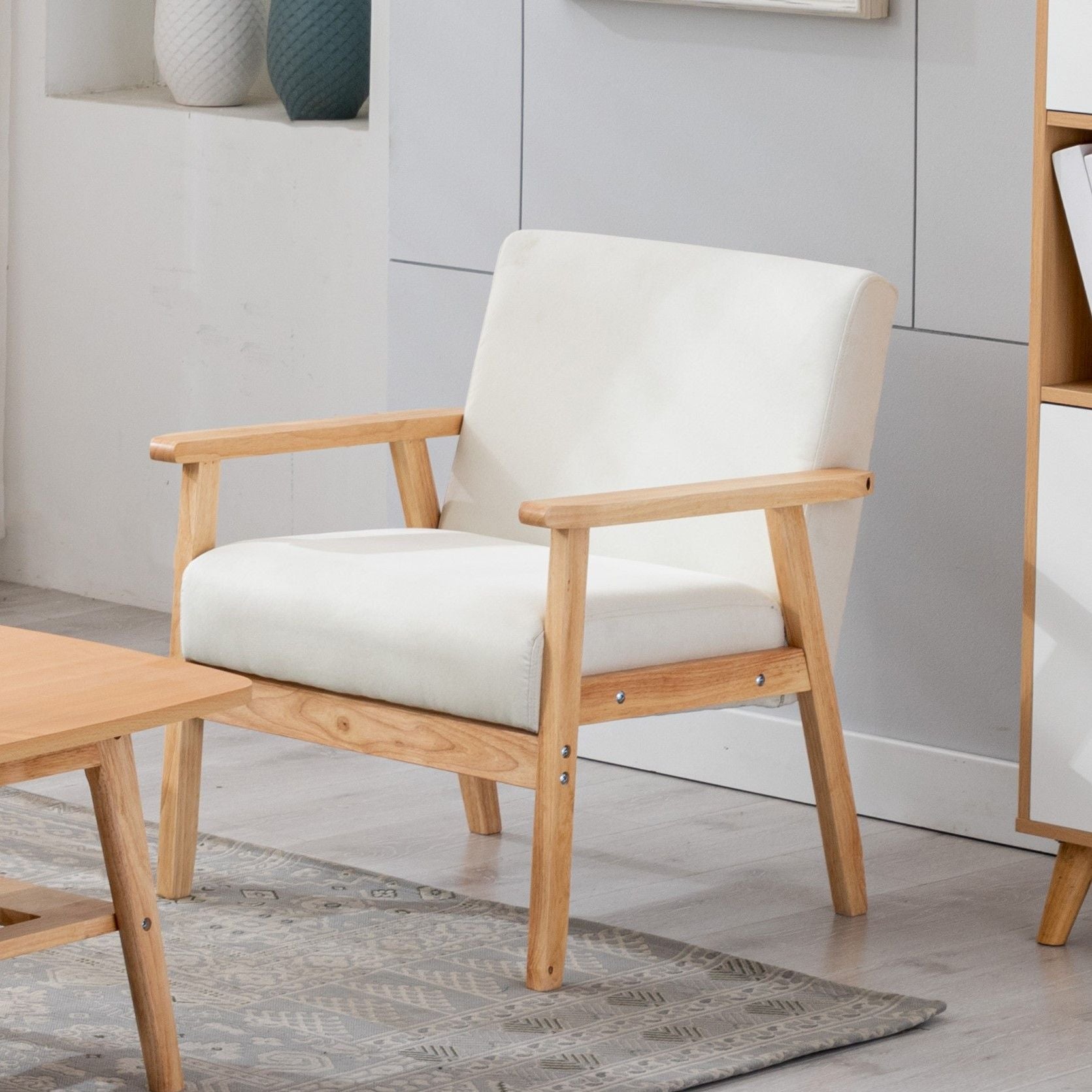 The Bahamas - Linen Fabric Chair, featuring a light wood frame and white cushioned seat and backrest, sits beside a wooden coffee table on a gray patterned rug in a bright, minimalistic room.