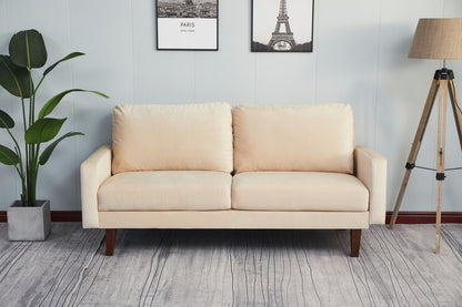 A Comfortable Sofa With Durable Construction and two cushions rests on a gray patterned rug. A potted plant stands left, a tripod floor lamp right, while two black-and-white pictures hang on the light blue wall behind.