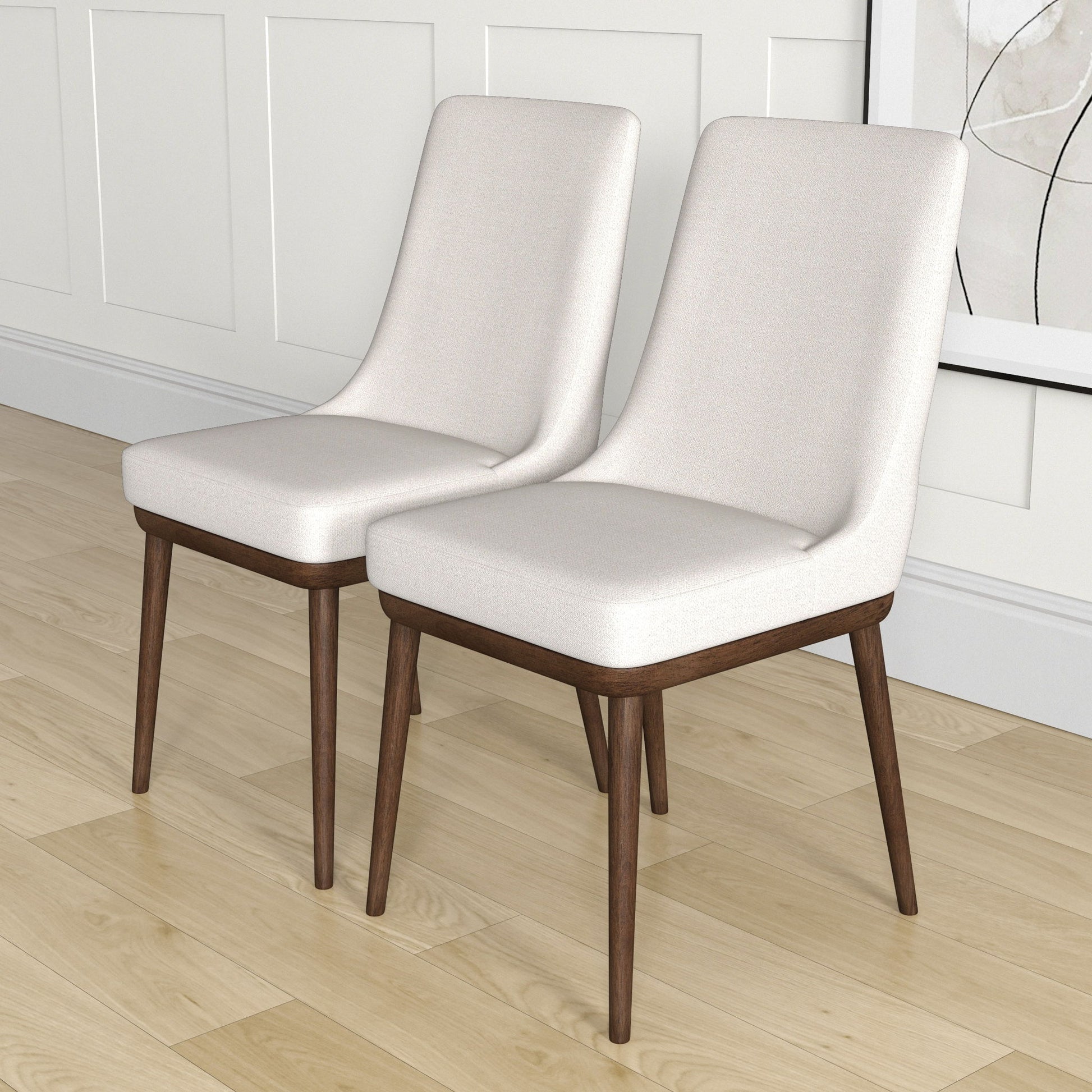 The Kate Mid-Century Modern Dining Chair set features two chairs with light beige upholstered seats and backs, angled dark wood legs, placed on a light wood floor near a white paneled wall and framed abstract art.