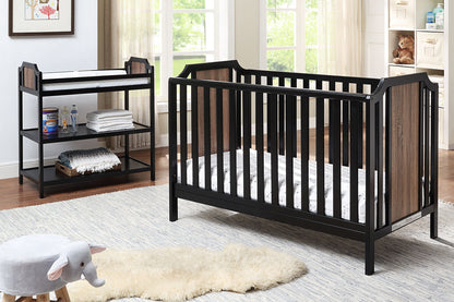 A modern nursery features a black and wood crib, the Brees Changing Table with baby supplies, a white rug, plush elephant stool, shelves of books and toys, and a large window filling the room with natural light.