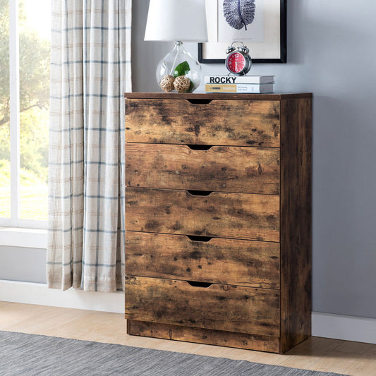 A 5 Drawer Bedroom Chest Dresser in distressed wood stands against the wall with a lamp, small plant, alarm clock, books, and a framed photo on top. A curtained window is to the left and a gray rug covers the floor.