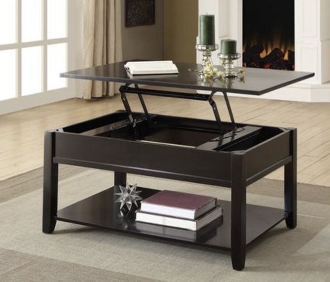 The Malachi Coffee Table With Lift Top in Black features a partially raised lift-top revealing interior storage. Books and decor rest on the lower shelf, while candles and a book sit atop. A fireplace appears in the background.