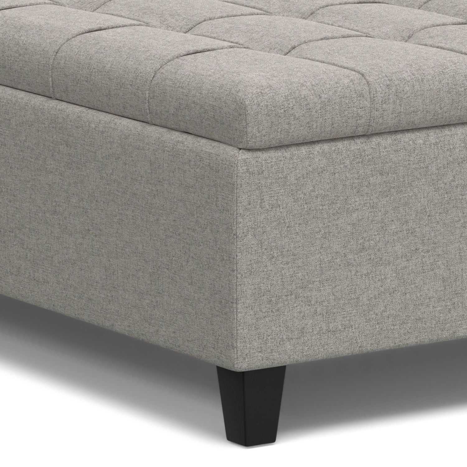 A close-up of the Harrison Upholstered Coffee Table Storage Ottoman shows its light gray tufted top and dark, tapered legs.