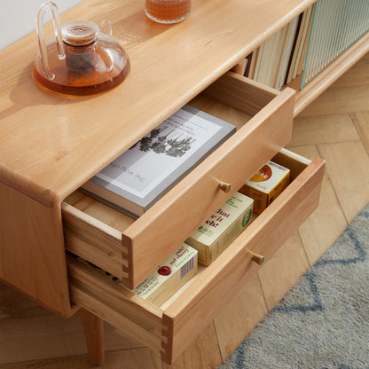A TV Cabinet with Chinese Changhong glass doors and two drawers holds a glass teapot, books, a magazine, and boxed teas. The cabinet stands on a wooden floor beside a blue rug and bookshelf.