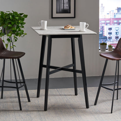 A Modern Bar Height Dining Table with a white laminate top and rubberwood legs is set with two white mugs and a pastry. Two brown chairs are beside it, with a potted plant and cityscape window in the background.