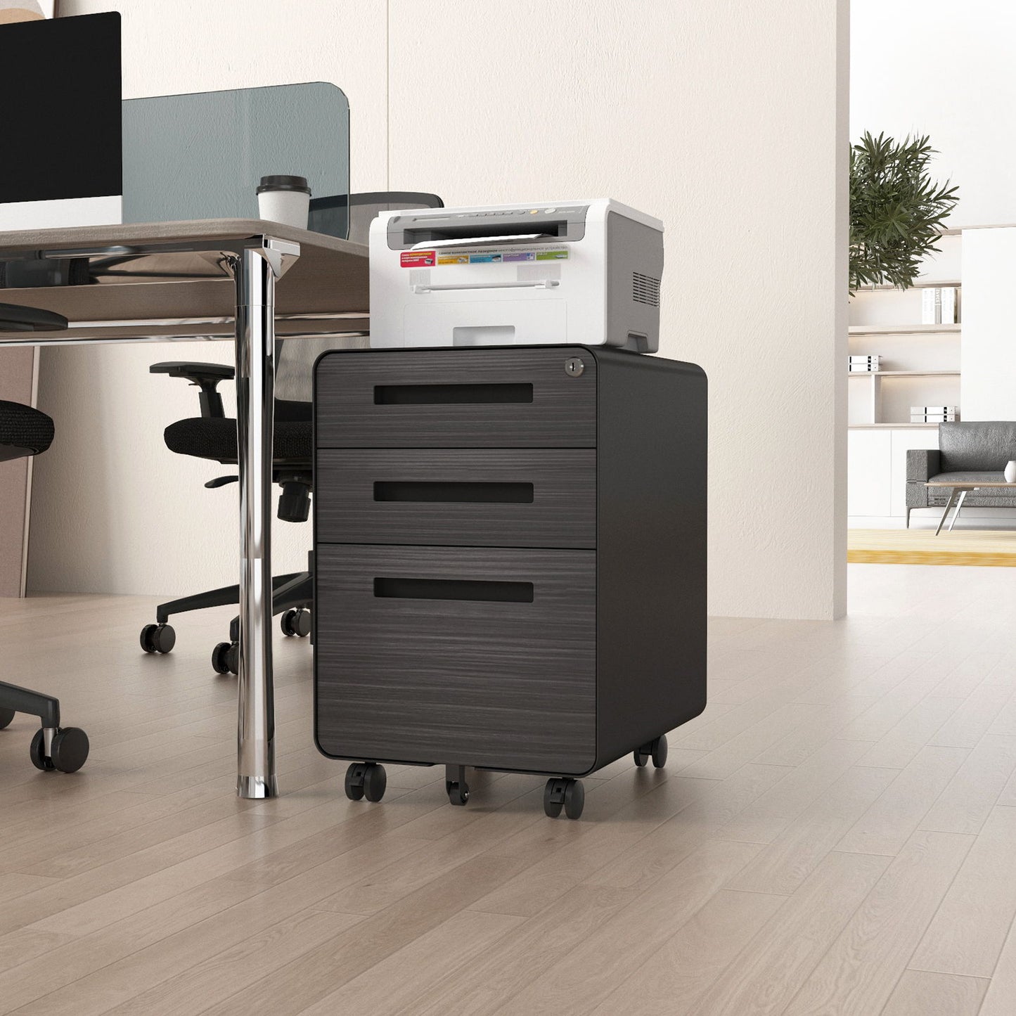 The 3 Drawer Mobile File Cabinet Under Desk Office, featuring a 5-wheel anti-tilting design and waterproof cold rolled steel, is placed by a desk in a bright office with a white printer on top; ergonomic chairs and decor are in the background.