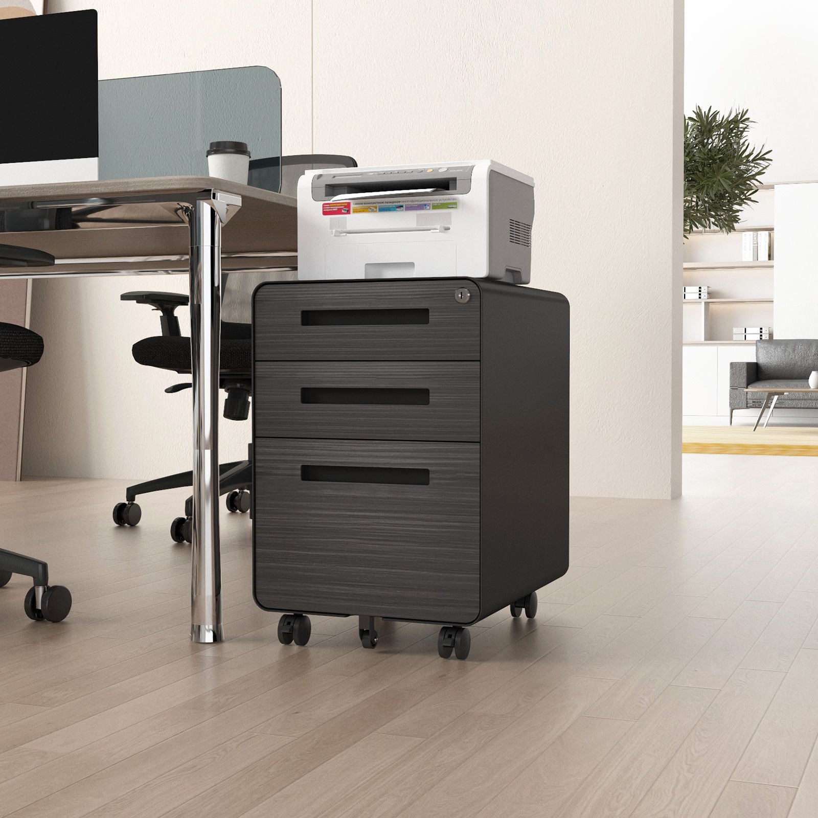 The 3 Drawer Mobile File Cabinet Under Desk Office, featuring a 5-wheel anti-tilting design and waterproof cold rolled steel, is placed by a desk in a bright office with a white printer on top; ergonomic chairs and decor are in the background.