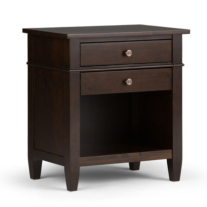 The Carlton - Bedside Table is a handcrafted dark wood nightstand with two drawers, an open middle shelf, sleek metal knobs, and tapered legs, shown on a white background.