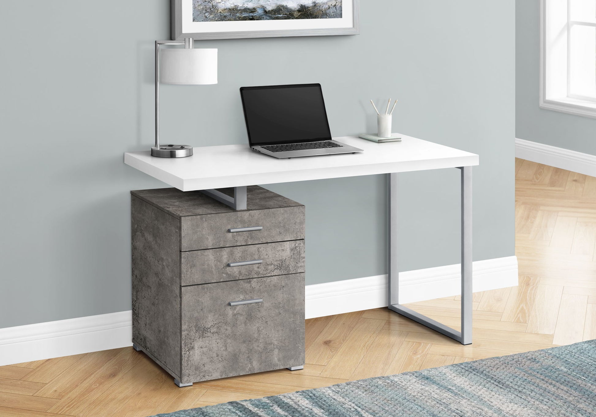 The Computer Desk Left Right Set-Up Storage Drawers For Home Office features a white tabletop, metal legs, and three gray drawers. It’s shown with a closed laptop, lamp, and pencil cup against a light gray wall on a wood floor.