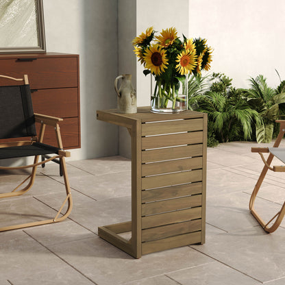 An Aluminum Outdoor C-Shaped Side Table for Patio displays a clear vase of sunflowers and a ceramic jug on a tiled patio, amidst chairs, greenery, and a brown cabinet.