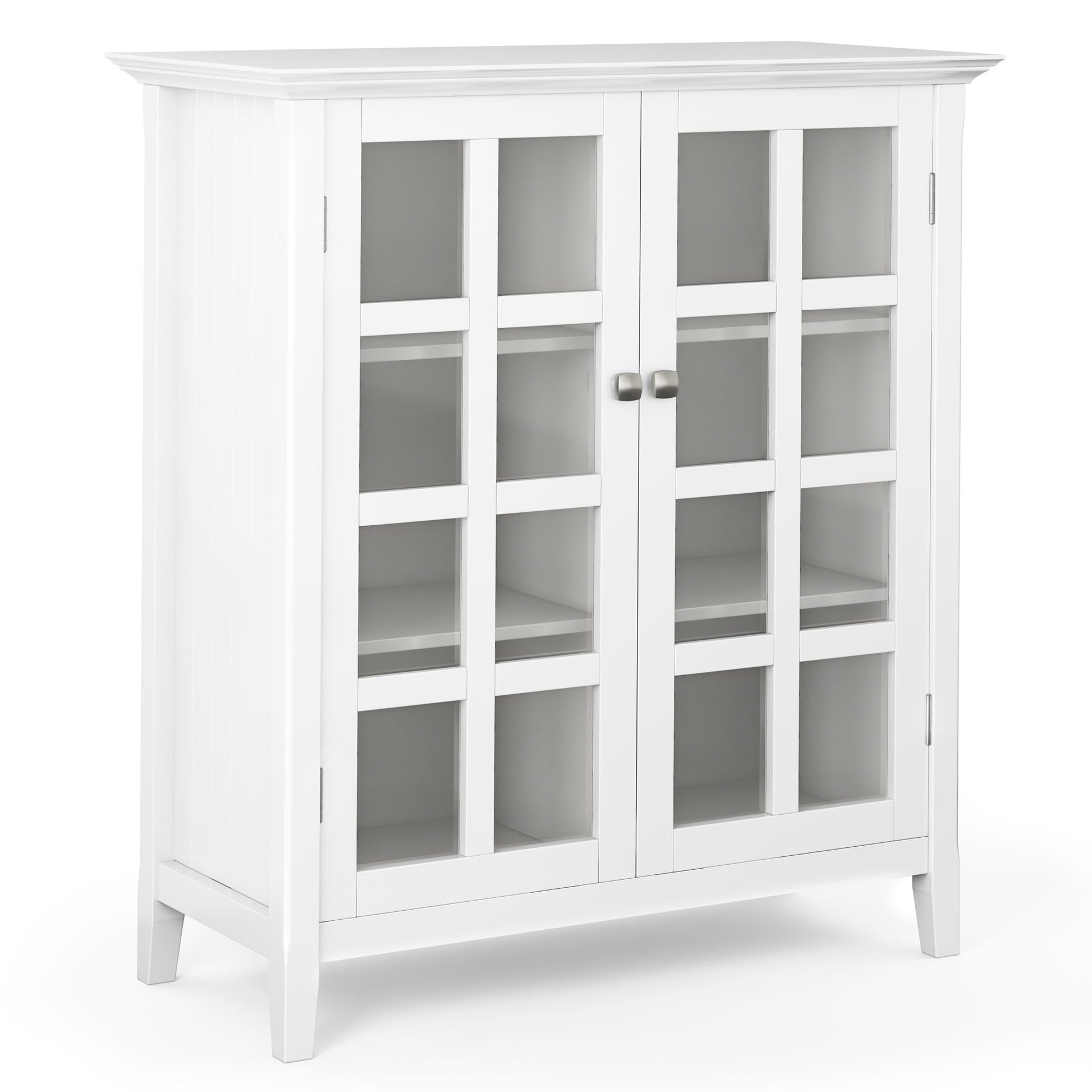 The Acadian - Medium Storage Cabinet is a handcrafted, white wooden piece with glass-paneled double doors, metal knobs, two interior shelves, and stands on four short legs in a simple modern design.