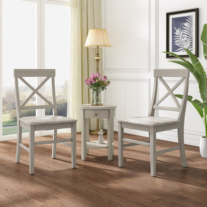 Two Plethora Dining Chairs with X-shaped backs (set of 2) in gray wood sit beside a small round white table with pink flowers, in a bright room featuring wood floors, large window, floor lamp, framed art, and a tall plant.