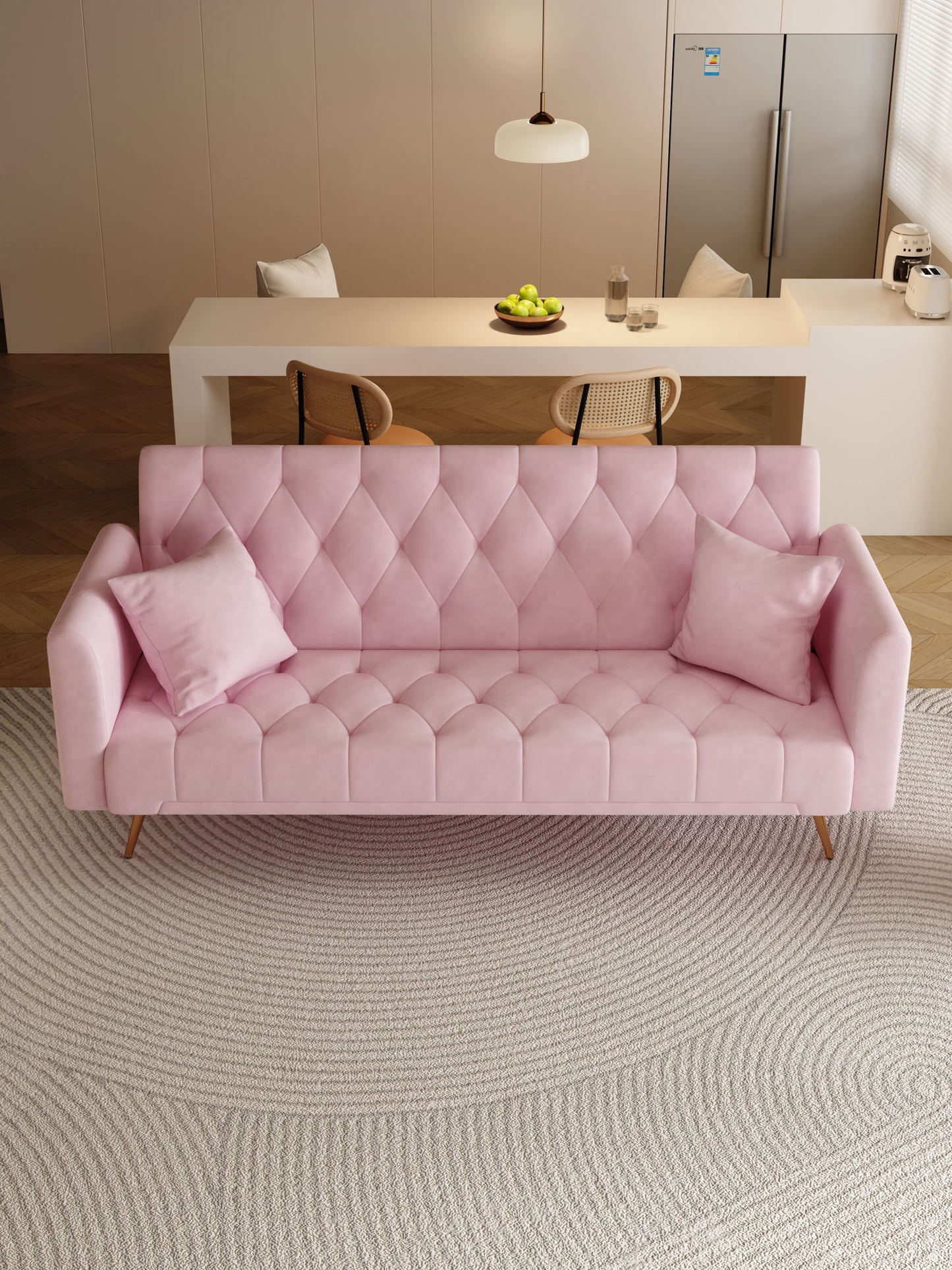 A modern living room features a pink Convertible Double Folding Living Room Sofa Bed with two matching pillows on a round textured rug. In the background are a dining table, chairs, bowl of green apples, pendant light, and refrigerator.