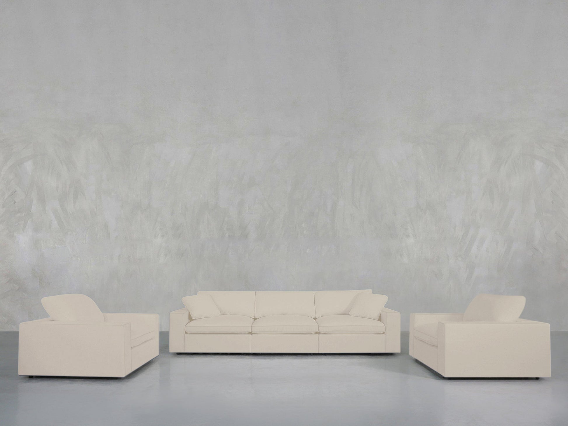 A minimalist living room features the 3-1-1 Sofa & Armchair Set, with a cream three-seater sofa and matching armchairs arranged on a smooth light floor against a textured light gray wall.