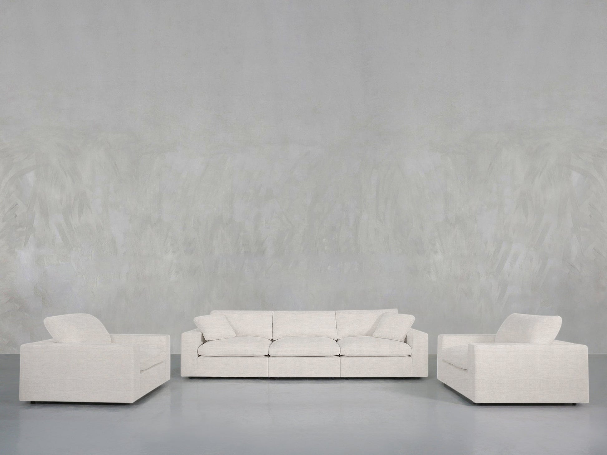 The 3-1-1 Sofa & Armchair Set, featuring a light gray sofa and two matching armchairs with clean lines and modern design, is arranged in a minimalist living room against a textured gray wall and floor.