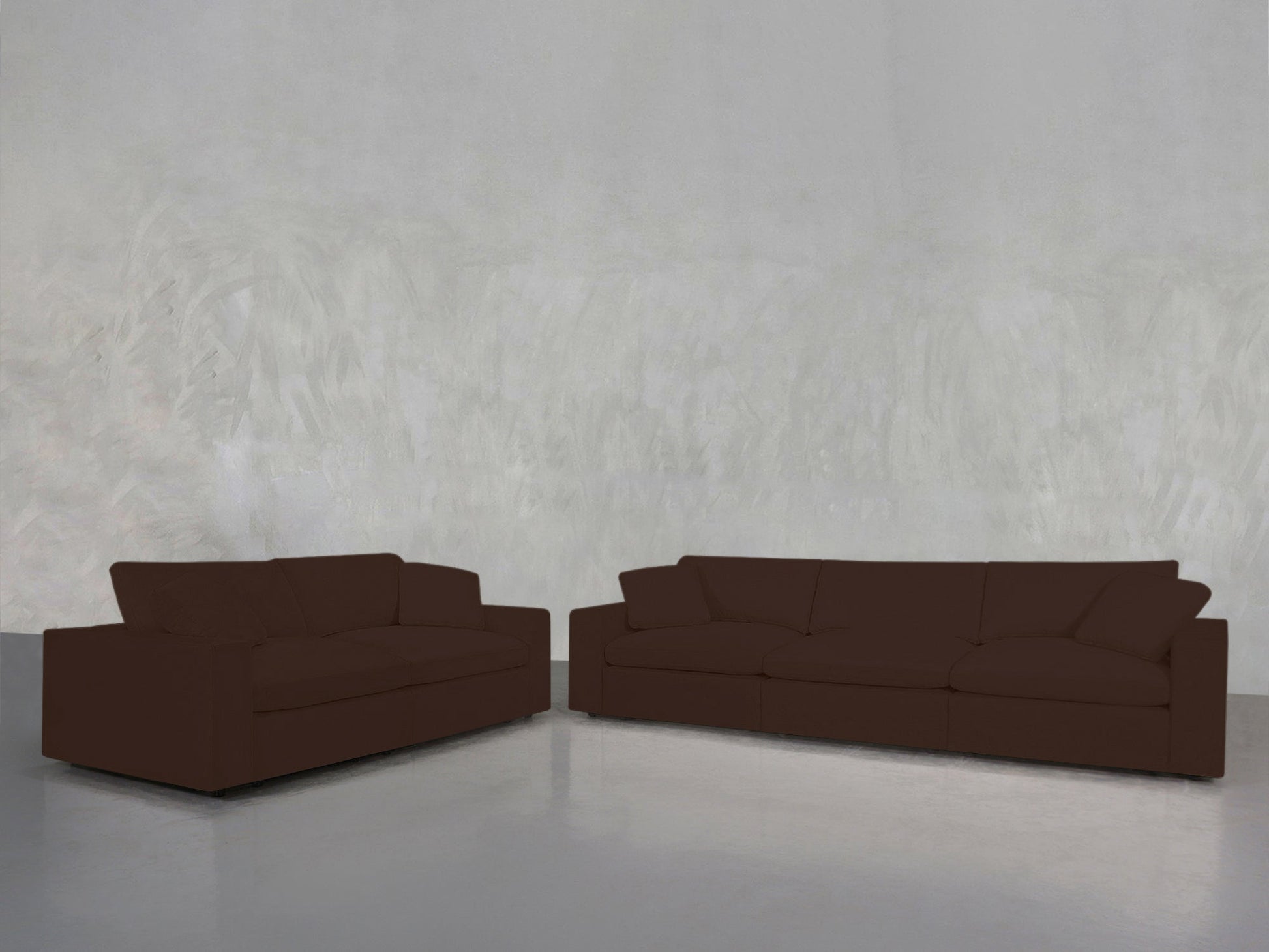 A 3-2 Sofa Set in dark brown is arranged against a plain, light gray textured wall on a shiny, light gray floor, creating a minimal and uncluttered setting.