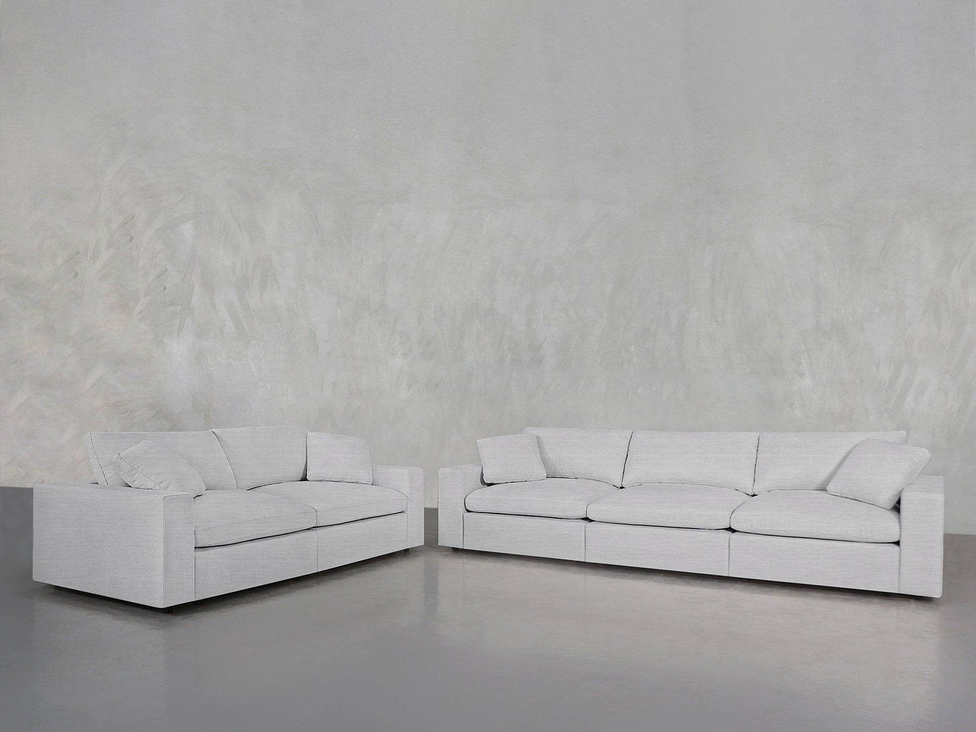 A 3-2 Sofa Set in modern light gray with clean lines and plush cushions is arranged in an L-shape against a minimalist, textured gray wall and polished gray floor.