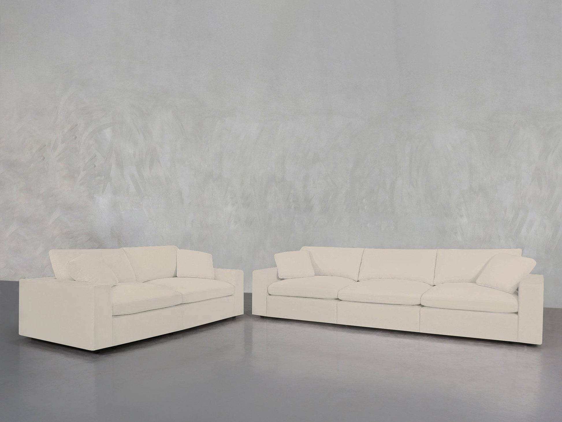 A minimalistic, uncluttered space features the 3-2 Sofa Set—two modern off-white sofas with clean lines—arranged on a polished concrete floor against a light gray textured wall.