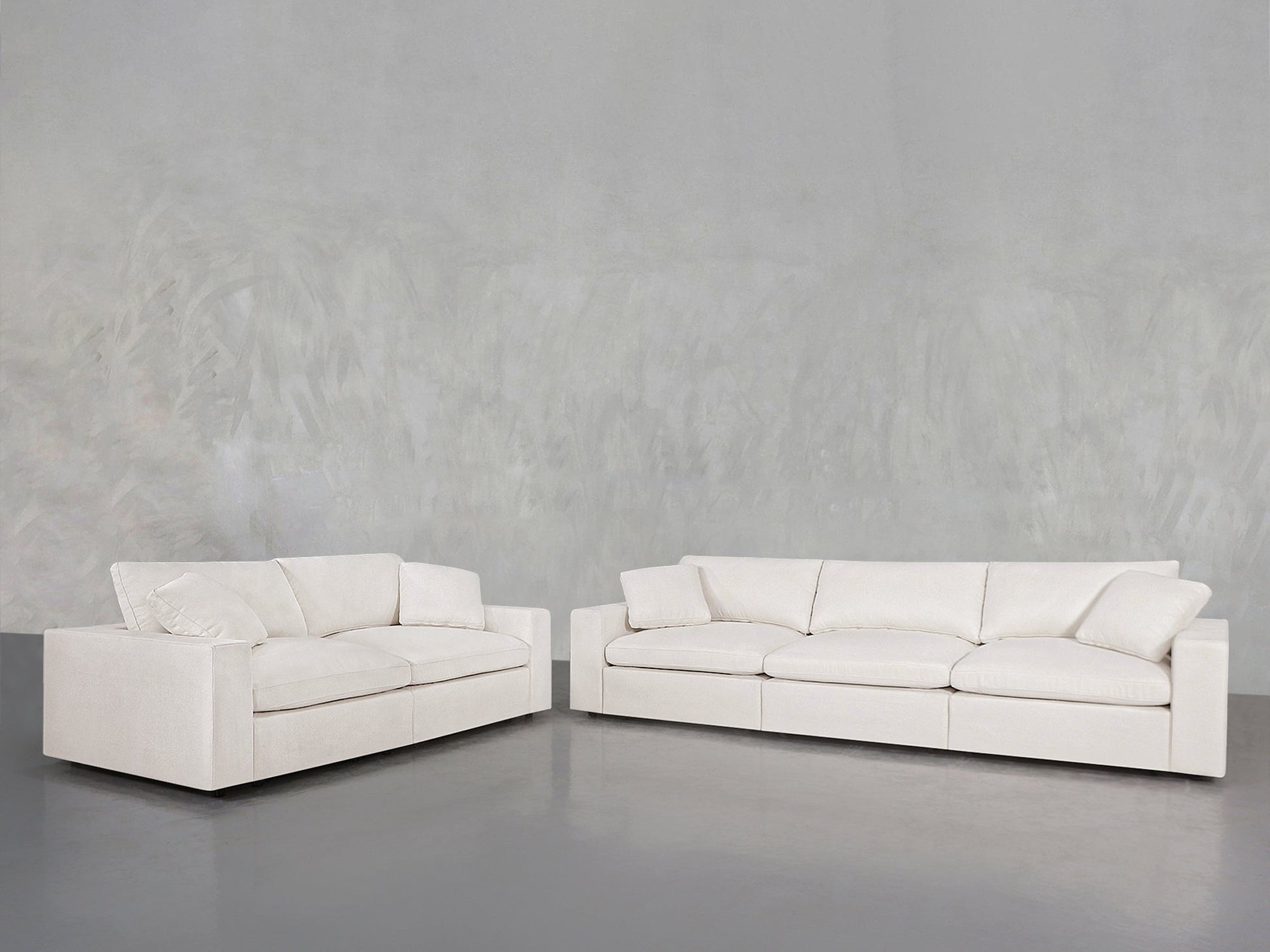 The 3-2 Sofa Set, featuring modern white upholstery with square arms and plush cushions, is arranged in an L-shape against a light gray textured wall and a smooth gray floor.