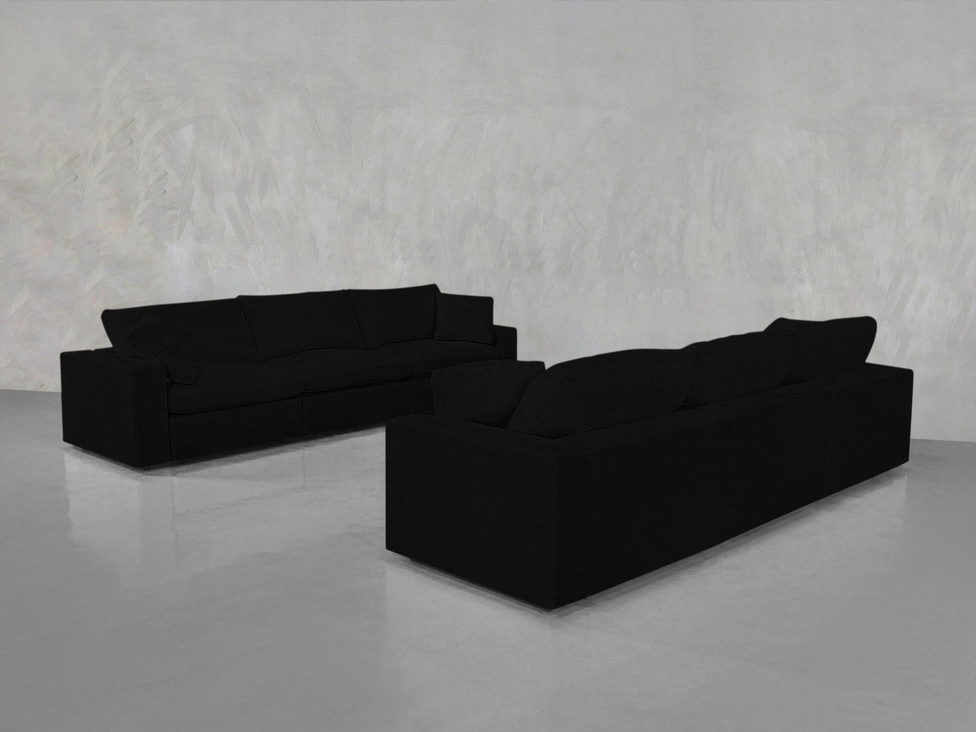Two 3-3 Sofa Sets in large black are arranged facing each other at an angle in an empty room with light gray textured walls and a shiny, reflective floor.