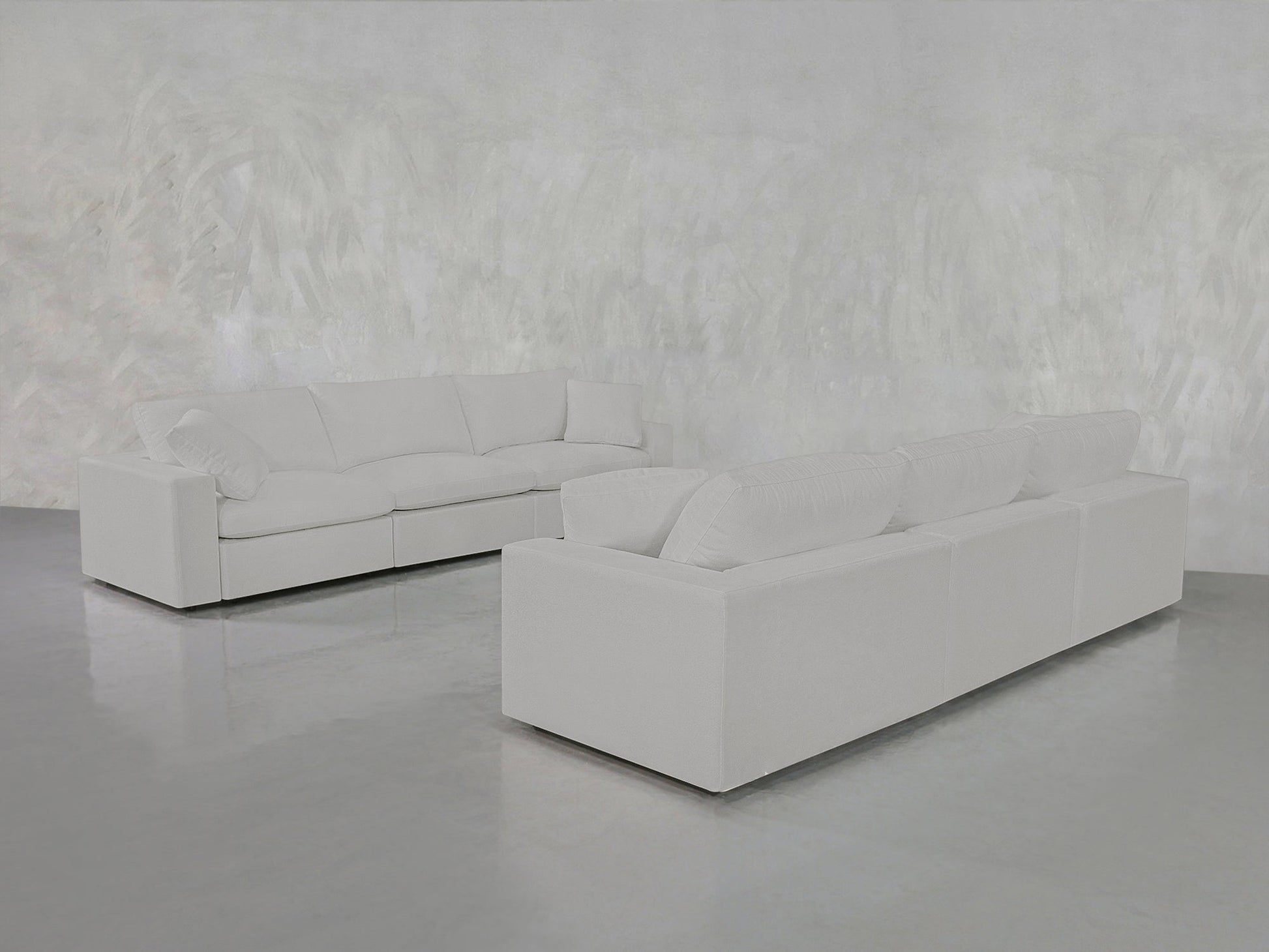 Two 3-3 Sofa Sets with clean lines are arranged in an L-shape in a minimalist room featuring a textured white wall and a shiny gray floor.