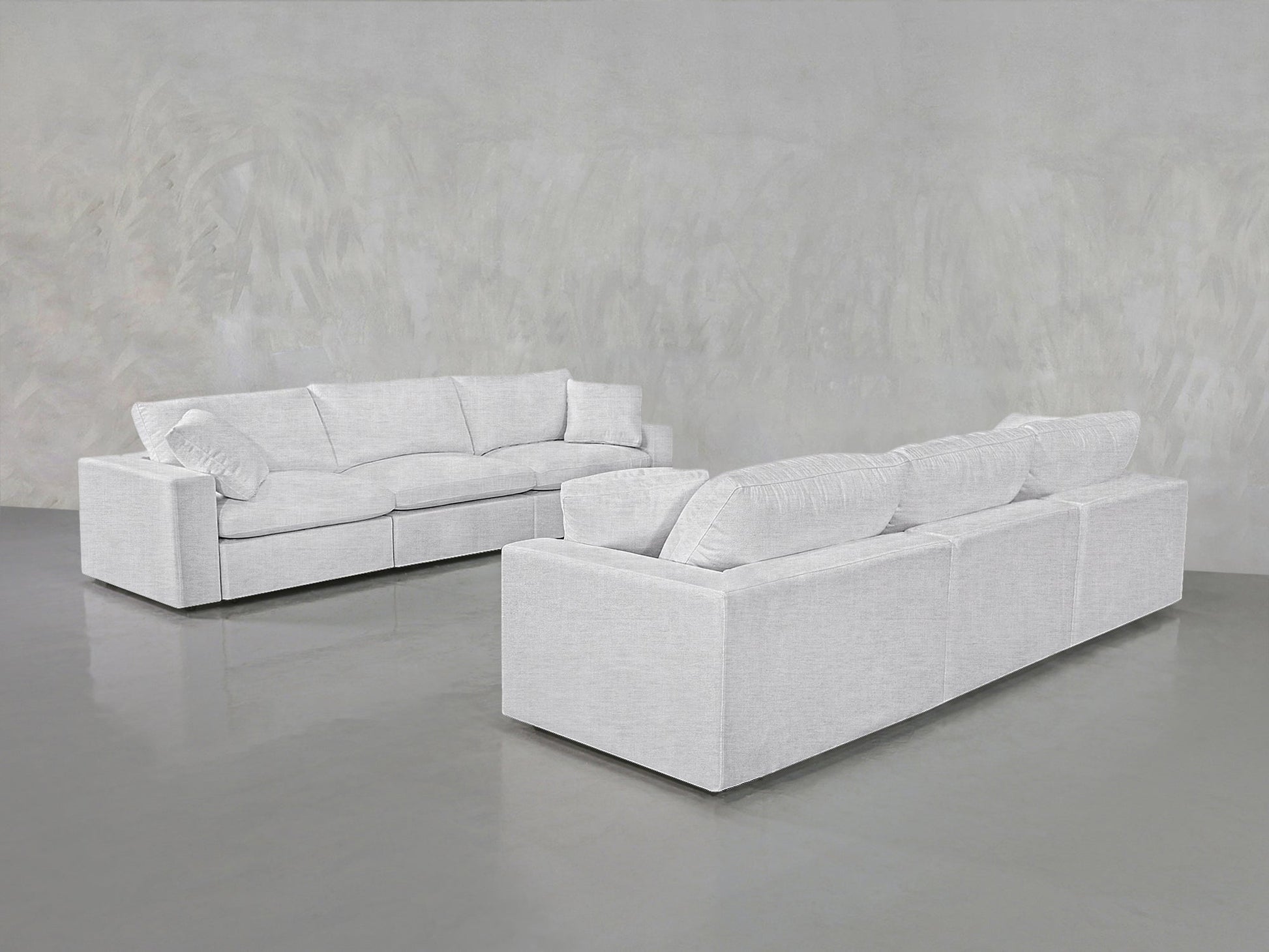 Two 3-3 Sofa Sets with plush cushions are arranged facing each other in a minimalist room featuring light gray walls and a glossy gray floor.