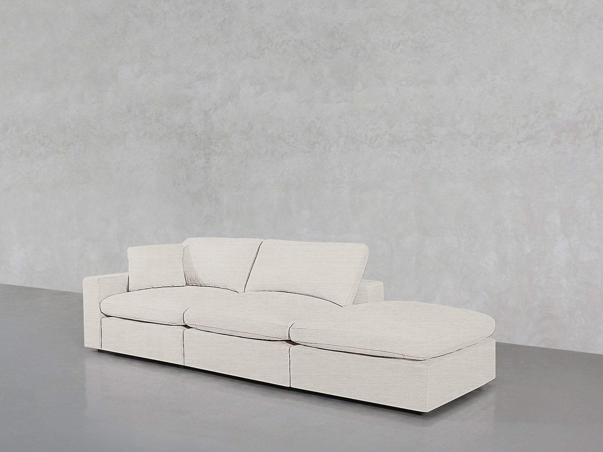 The 3-Seat Modular Lounger Sofa features a modern light beige design with three seat cushions, a right-side chaise, and low square armrests, set against a plain light gray textured wall and gray flooring.