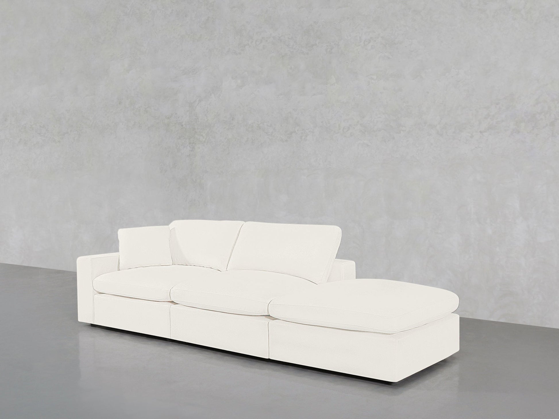 The 3-Seat Modular Lounger Sofa in modern white with a chaise lounge is placed on a polished gray floor against a light gray textured wall.