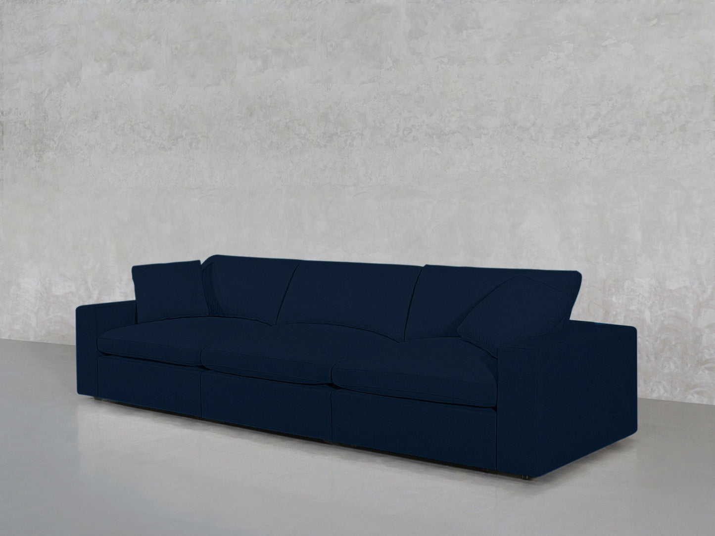 A 3-Seat Modular Sofa in modern dark blue, featuring clean lines, is placed before a light gray textured wall on a smooth, light gray floor for a minimalist, uncluttered look.