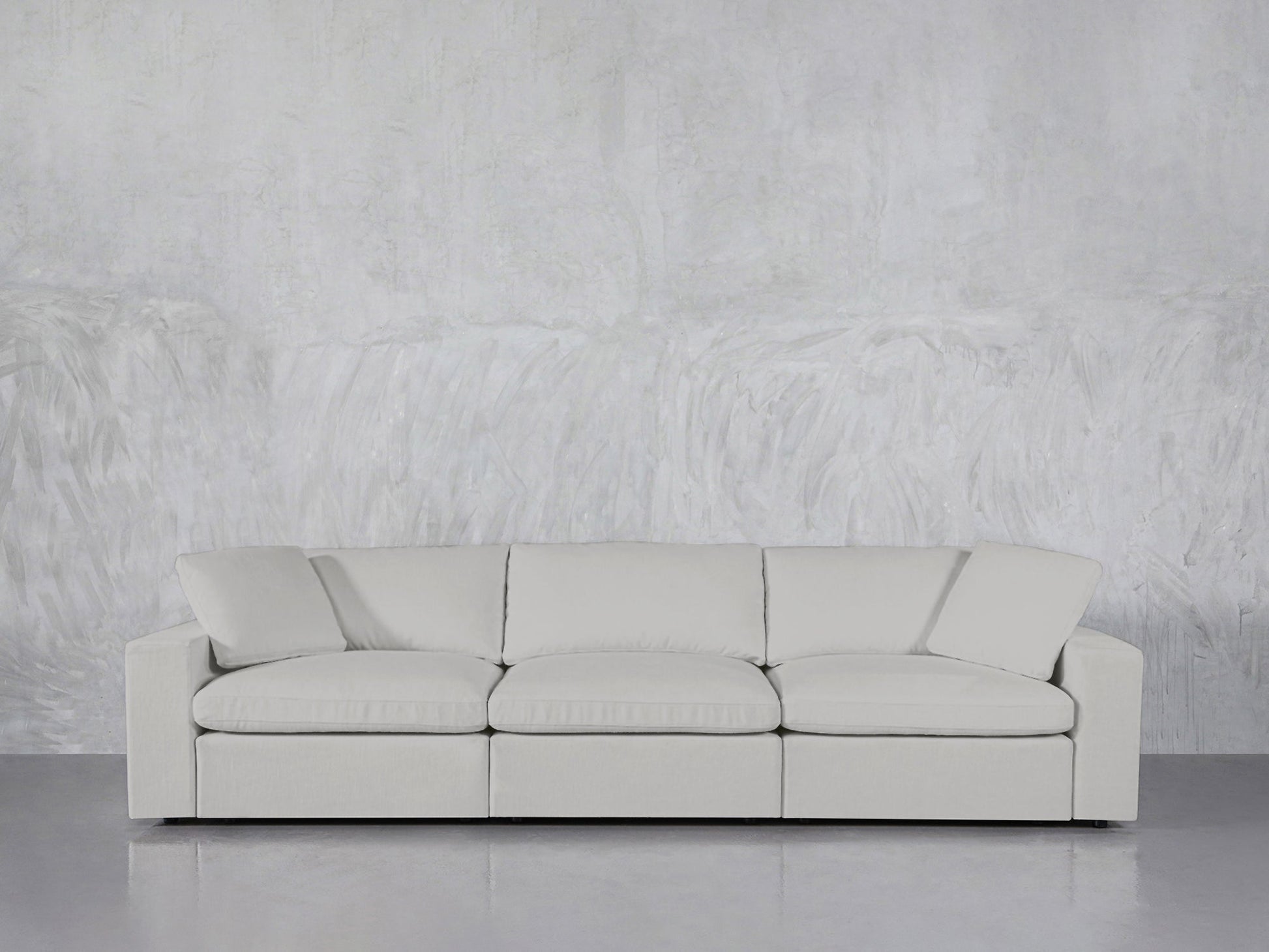 The 3-Seat Modular Sofa, featuring modern clean lines in light gray, sits against a textured gray wall atop a glossy floor.