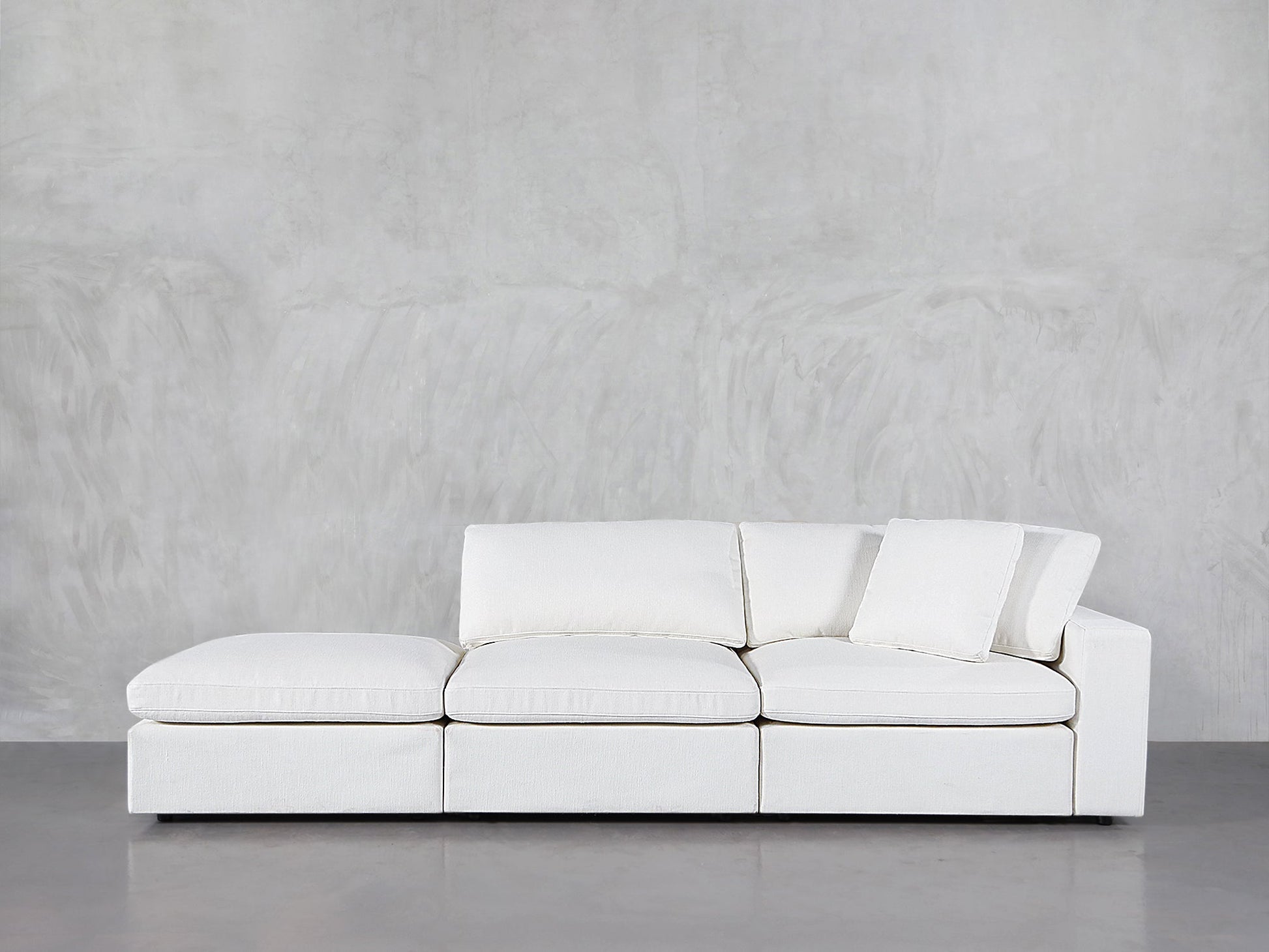 The 3-Seat Modular Lounger Sofa, upholstered in modern white with three seat and back cushions plus a matching throw pillow, sits against a light gray textured wall on a polished floor.