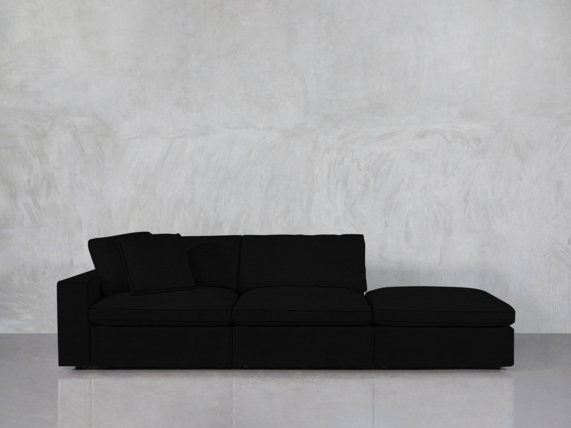 The 3-Seat Modular Lounger Sofa, featuring a sleek black finish and right-side chaise, is showcased against a light gray textured wall and a pale floor.