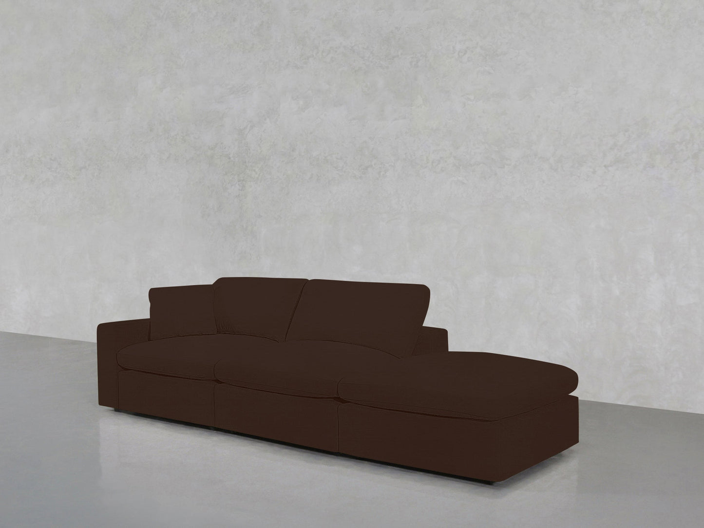 A 3-Seat Modular Lounger Sofa with a right-side chaise, finished in dark brown, sits against a light gray textured wall on a smooth, light floor.