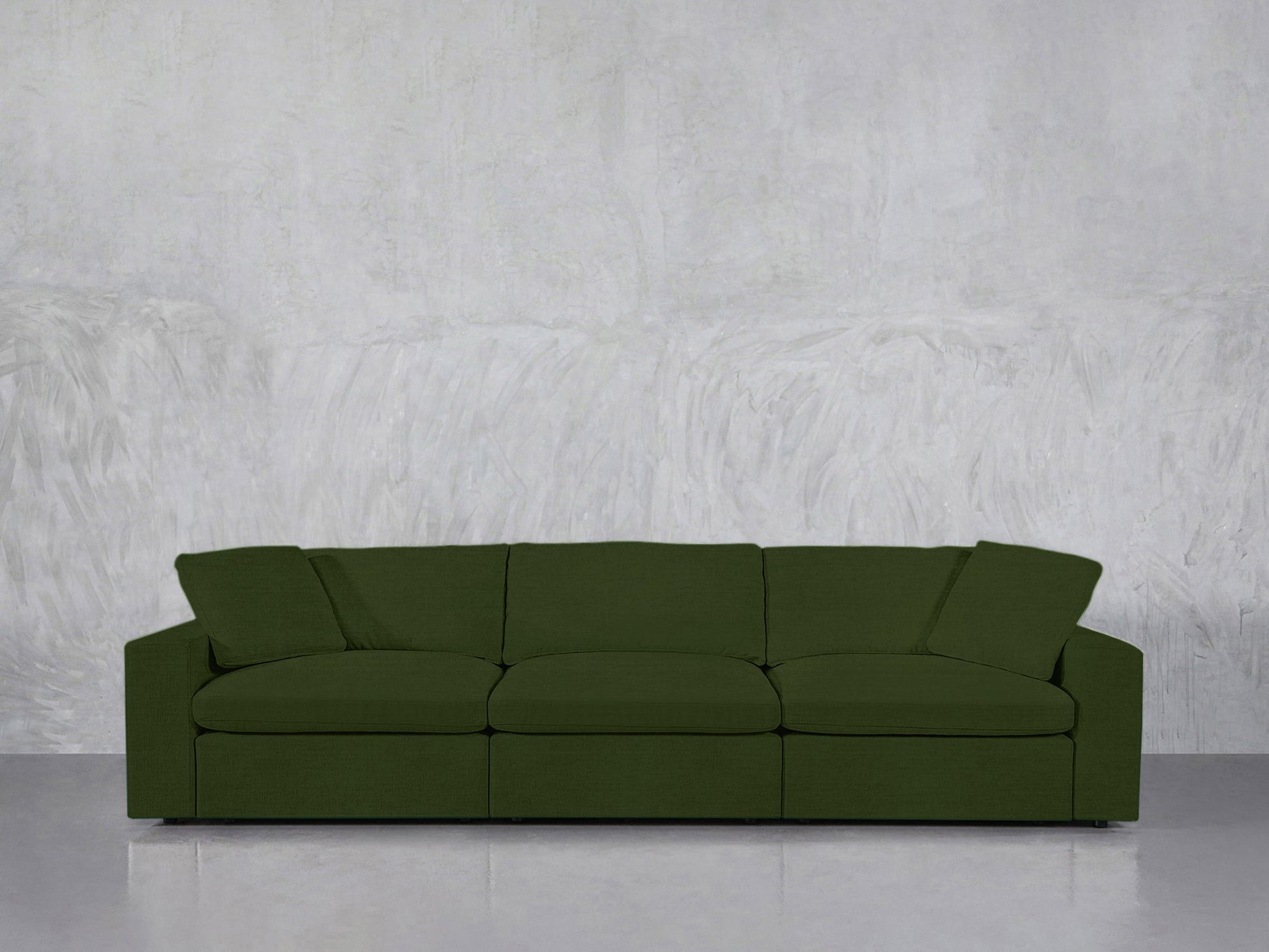 A 3-Seat Modular Sofa in dark green sits against a light gray textured wall on a shiny, light-colored floor. It features wide armrests and plush cushions.