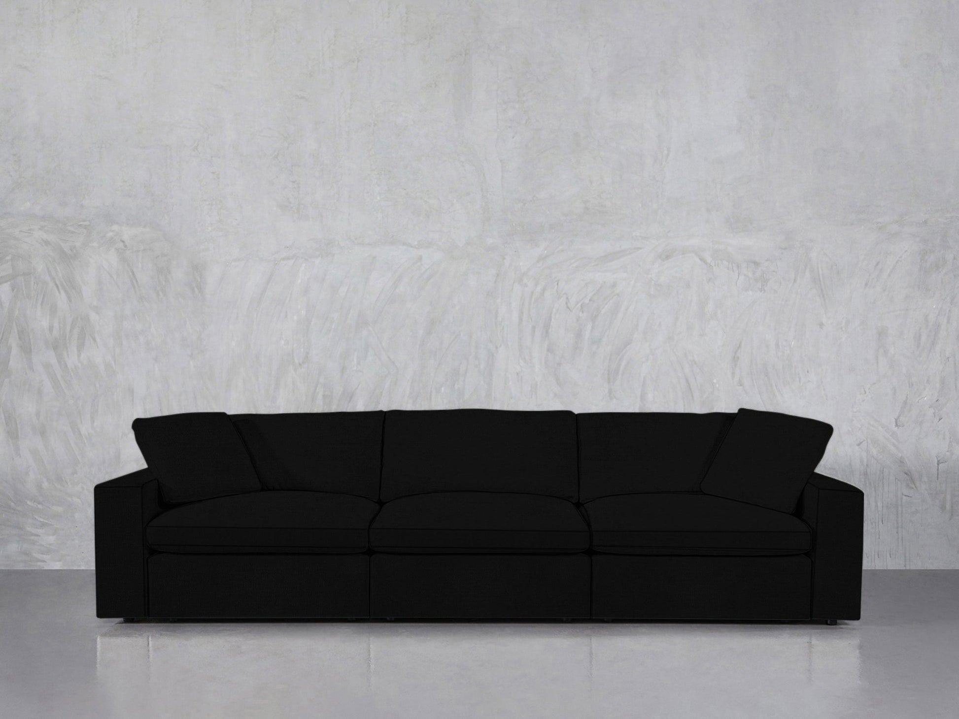 The 3-Seat Modular Sofa, in modern black with three cushions and two armrests, is set against a light gray textured wall on a smooth, reflective floor.