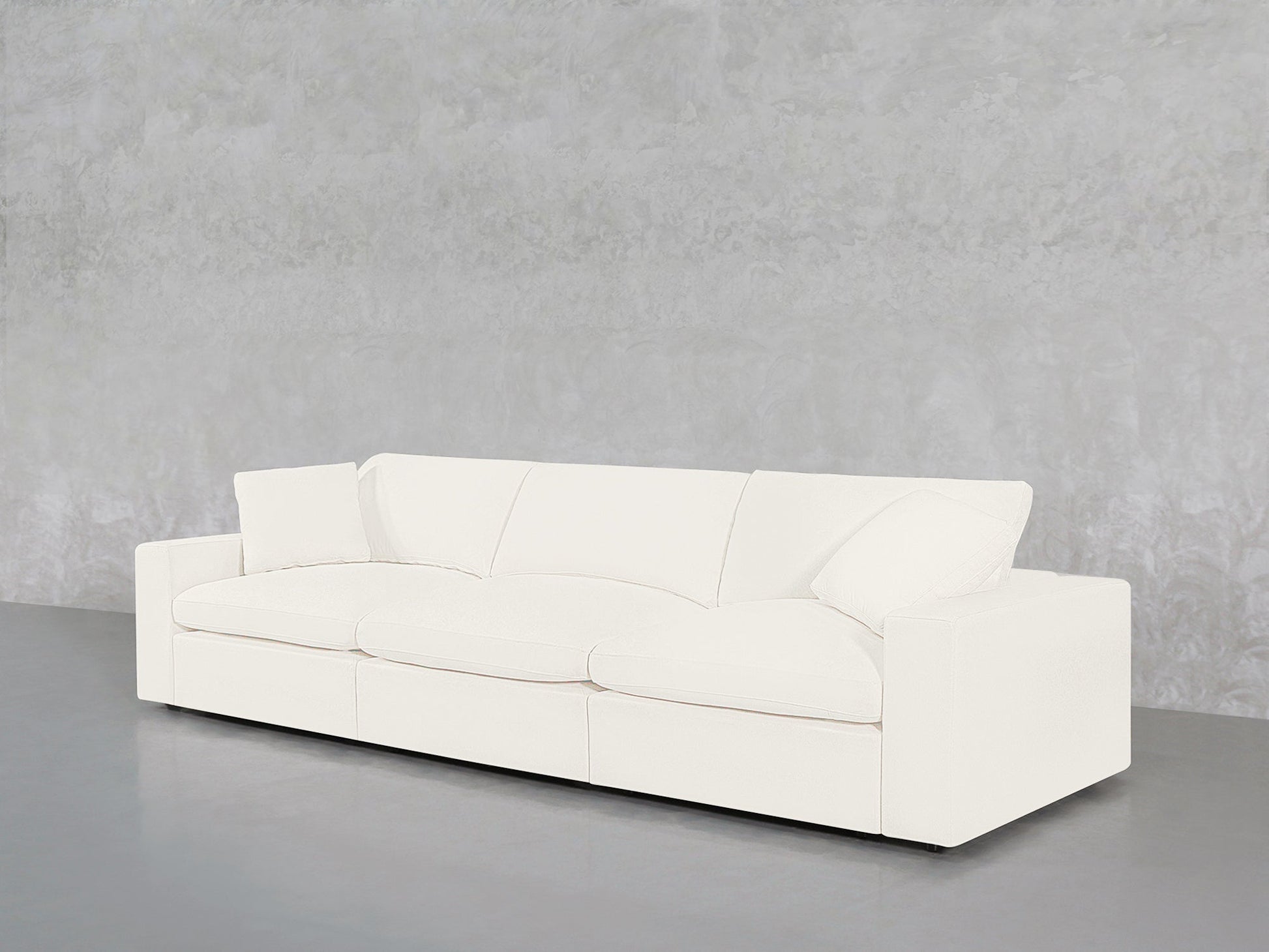 The 3-Seat Modular Sofa with clean lines and plush cushions is placed against a light gray textured wall and set on a smooth, gray floor.
