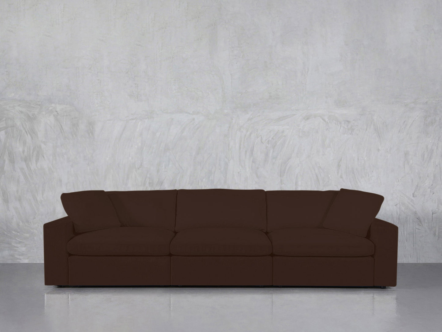 A 3-Seat Modular Sofa in dark brown, featuring wide armrests and plush cushions, sits against a light gray textured wall on a smooth, reflective floor.