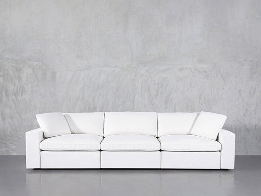 A 3-Seat Modular Sofa in modern white, featuring straight arms and three seat cushions, sits against a light gray textured wall on a shiny gray floor.