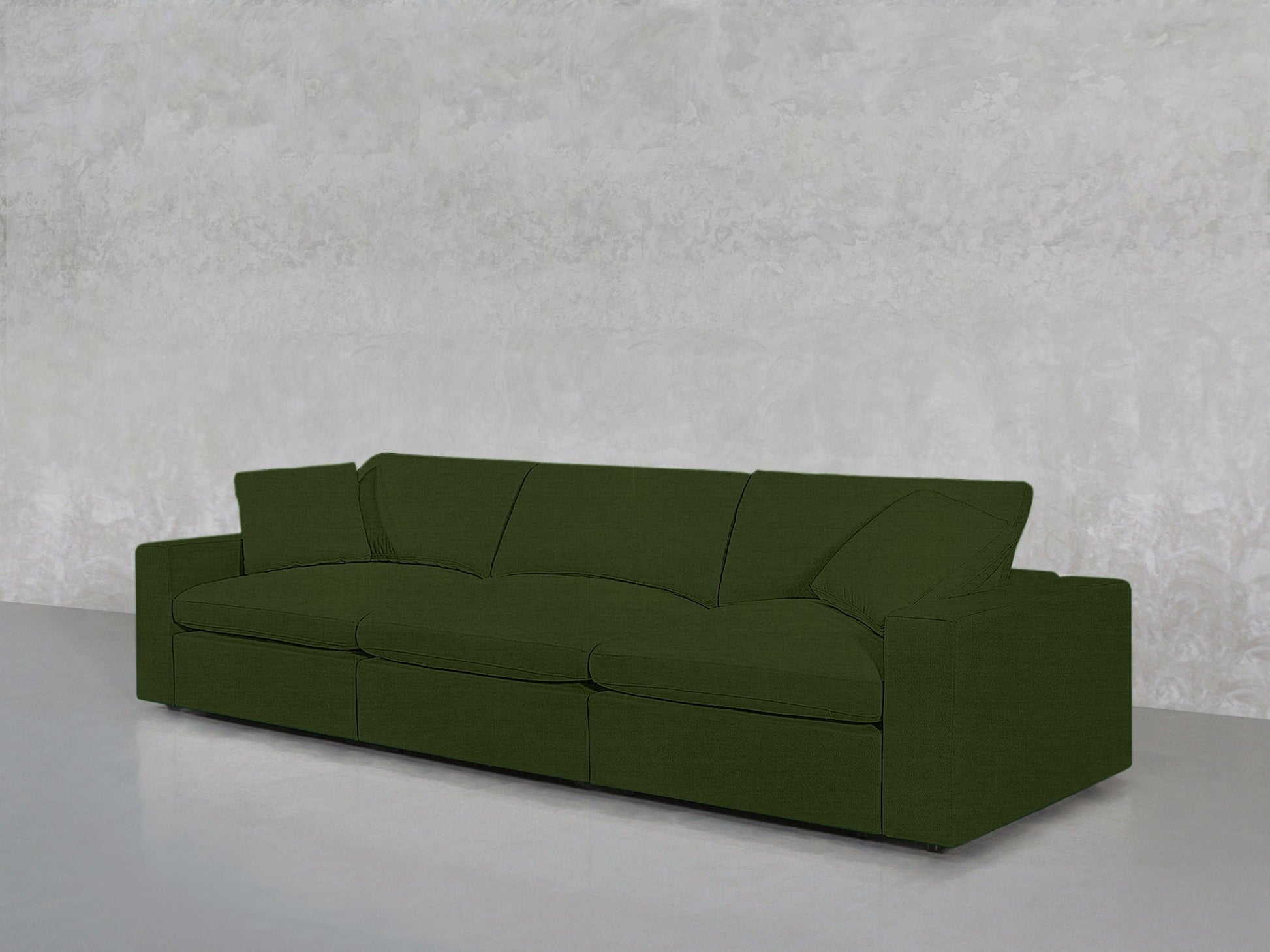 The 3-Seat Modular Sofa in dark green, featuring wide armrests, stands against a light gray textured wall on a smooth, light gray floor.