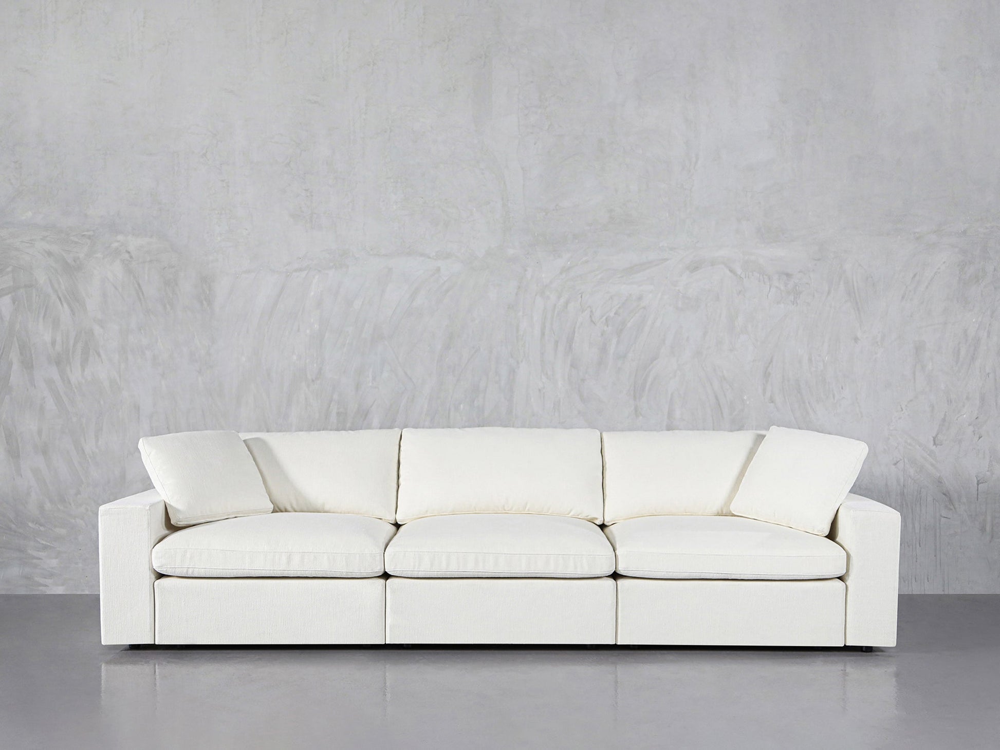 The 3-Seat Modular Sofa with clean lines and plush cushions, in modern white, is set against a light gray textured wall on a smooth gray floor.
