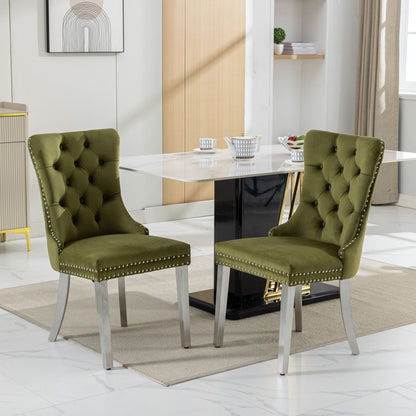 Two Nikki modern tufted velvet dining chairs with chrome stainless steel legs and nailhead trim are placed on a beige rug in a bright dining room with a white marble table and contemporary decorative accents in the background.