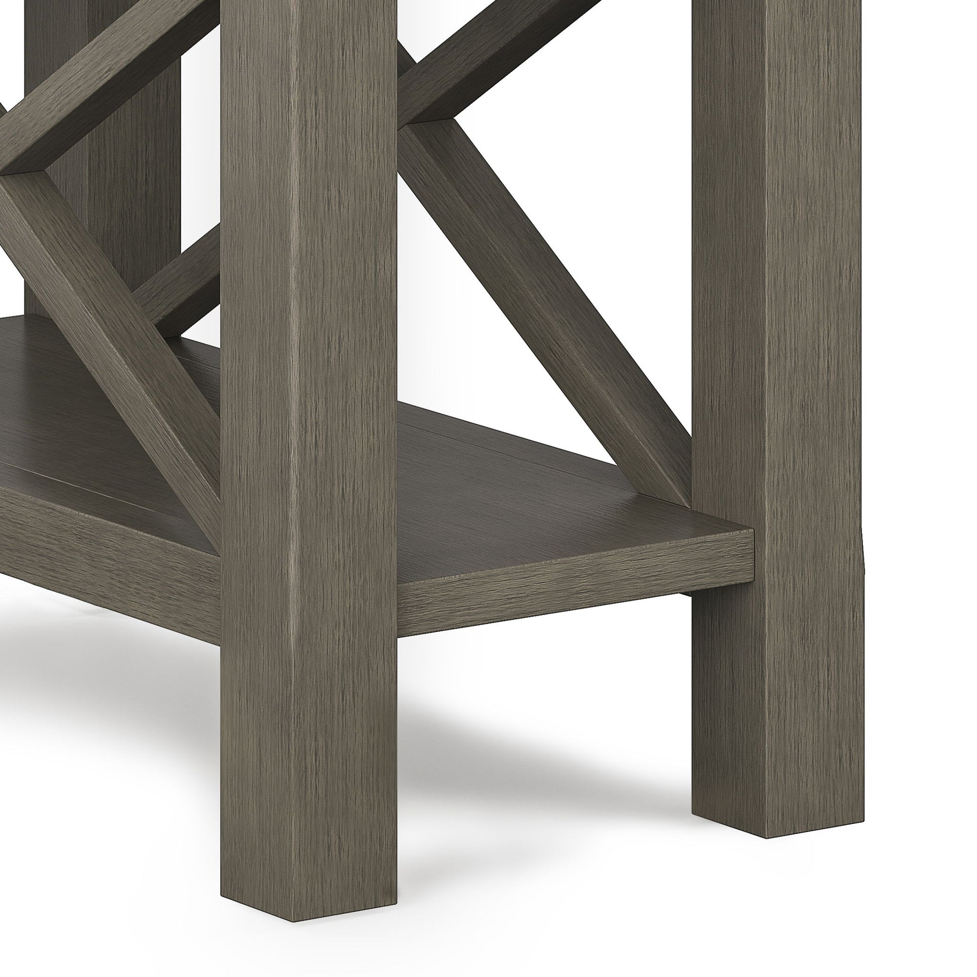Close-up of the Kitchener - Handcrafted Table’s corner and legs with a grayish-brown finish, lower shelf, and crisscross support beams in the background.