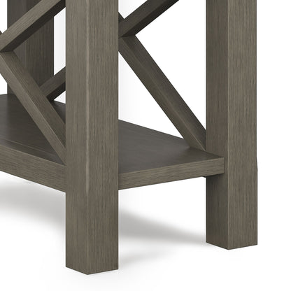 Close-up of the Kitchener - Handcrafted Table’s corner and legs with a grayish-brown finish, lower shelf, and crisscross support beams in the background.