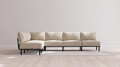 An Indoor Jack 6-Seater Open-Ends Corner Sectional in Balsa, featuring black legs, is elegantly positioned on a light gray rug against a plain white wall. The sectional is configured in an L-shape, enhancing the room's modern and minimalist appeal.
