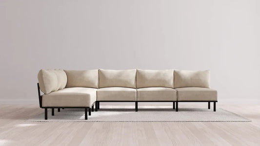 An Indoor Jack 6-Seater Open-Ends Corner Sectional in Balsa, featuring black legs, is elegantly positioned on a light gray rug against a plain white wall. The sectional is configured in an L-shape, enhancing the room's modern and minimalist appeal.